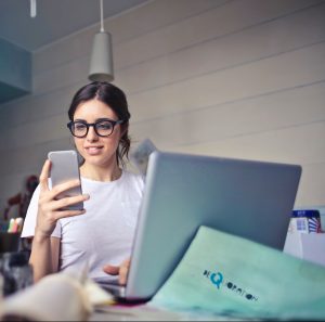 woman in white t shirt holding smartphone in front of laptop