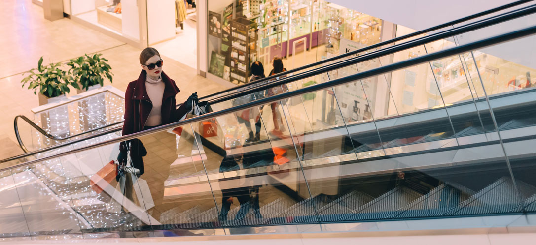 Woman riding up escalator with shopping bags in retail center