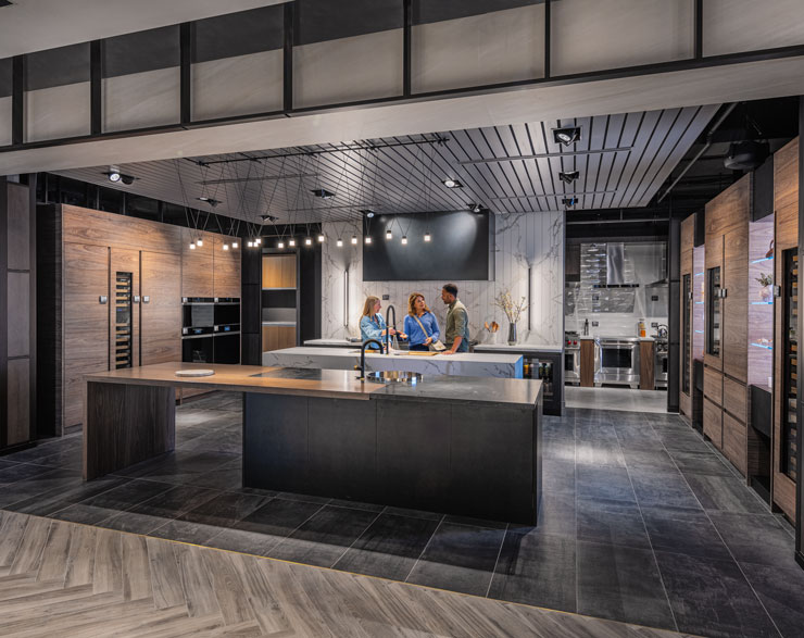 Customer, architect, and employee discussing products in a dark-themed kitchen display at Ferguson Studio Showroom