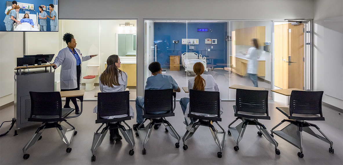 Three students listen to an instructor walk through a health simulation.