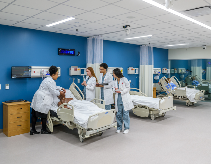 Three students watch their instructor as she demonstrates patient care.