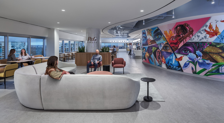 Employees talk on couches in an open office area with a colorful mural in the background