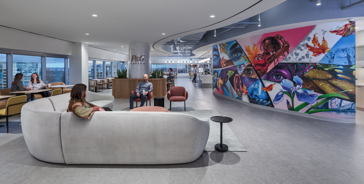 Employees talk on couches in an open office area with a colorful mural in the background