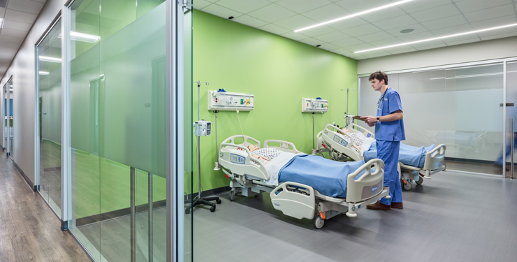 A nursing student stands at a simulated patient's bedside