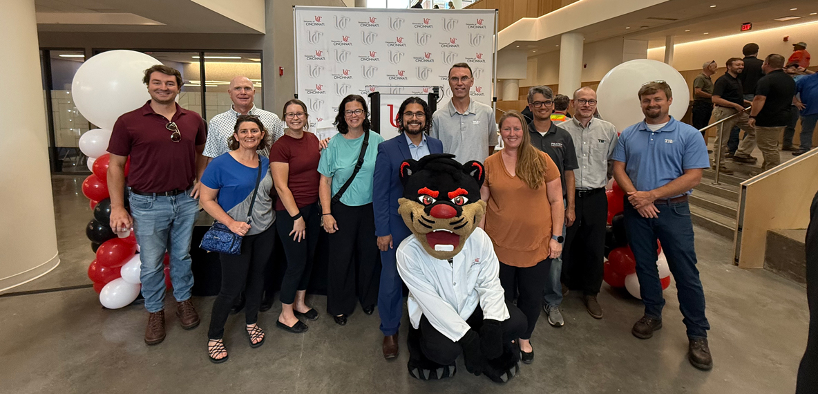 A group of people stand in front of a UC-branded step and repeat banner
