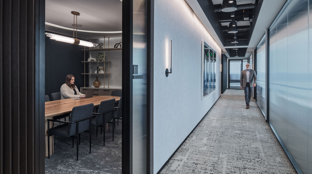 Women working in a room, man walkin in the hall