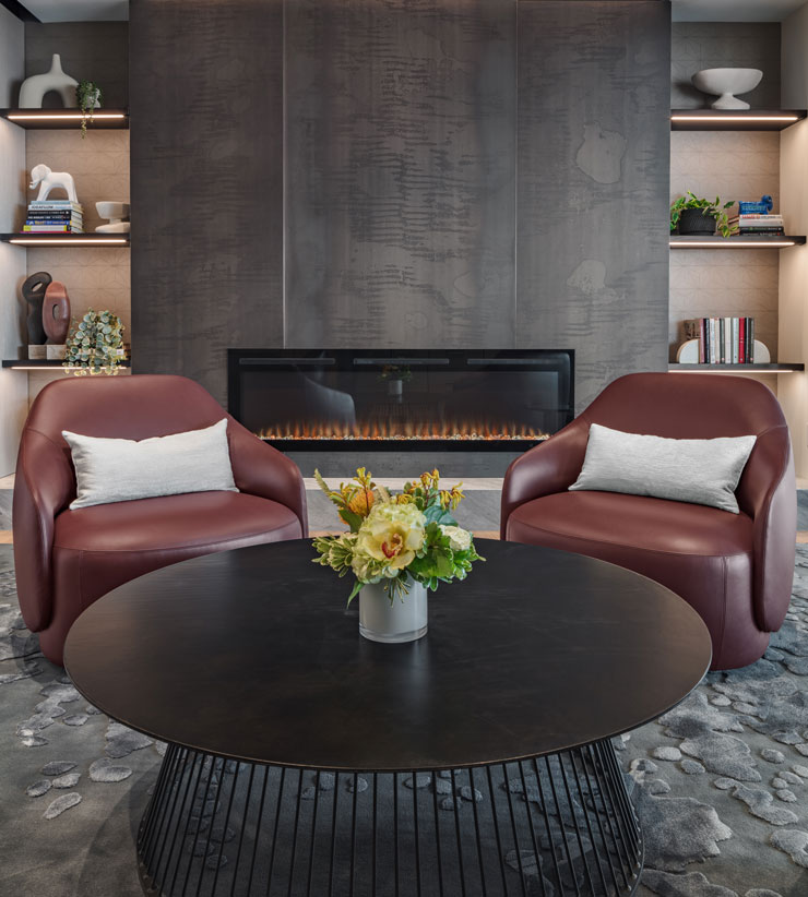 Two brown leather chairs infornt of a fire place, behind a black table with bright yellow flowers on it.