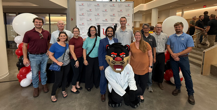 A group of people stand in front of a UC-branded step and repeat banner