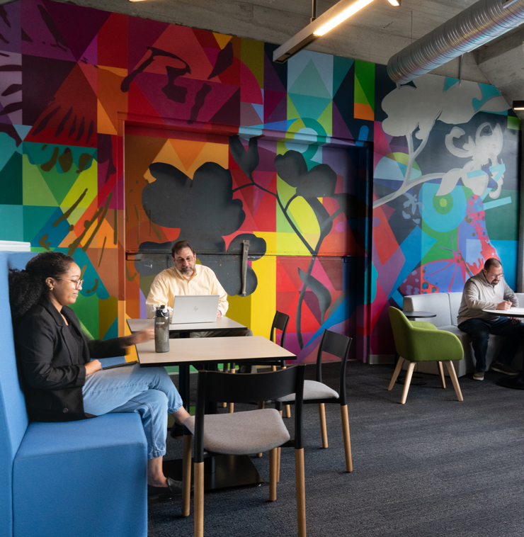 Employees work together in the Commons—a collaborative space backed by a colorful mural. 