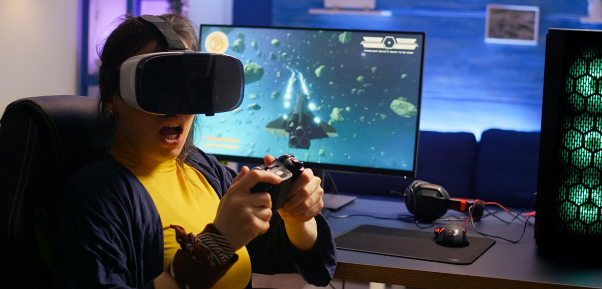 A woman wears a VR headset and sits at a computer