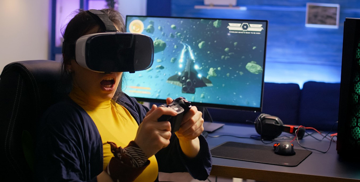 A woman wears a VR headset and sits at a computer