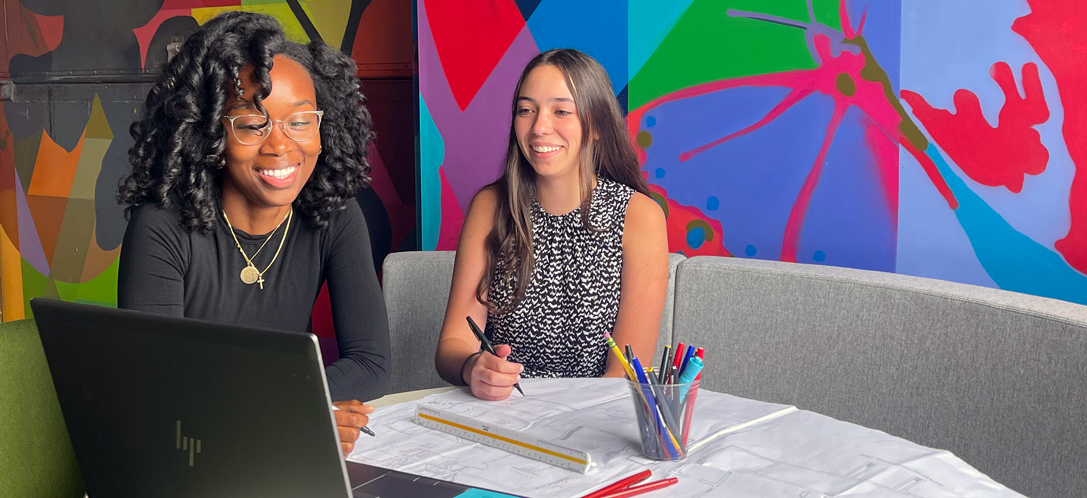 Two interns sit together at a table in the Commons