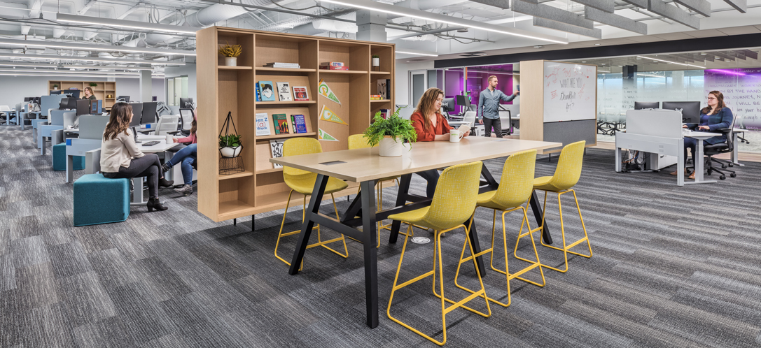 An employee is working solo at a high-top table in a busy workplace