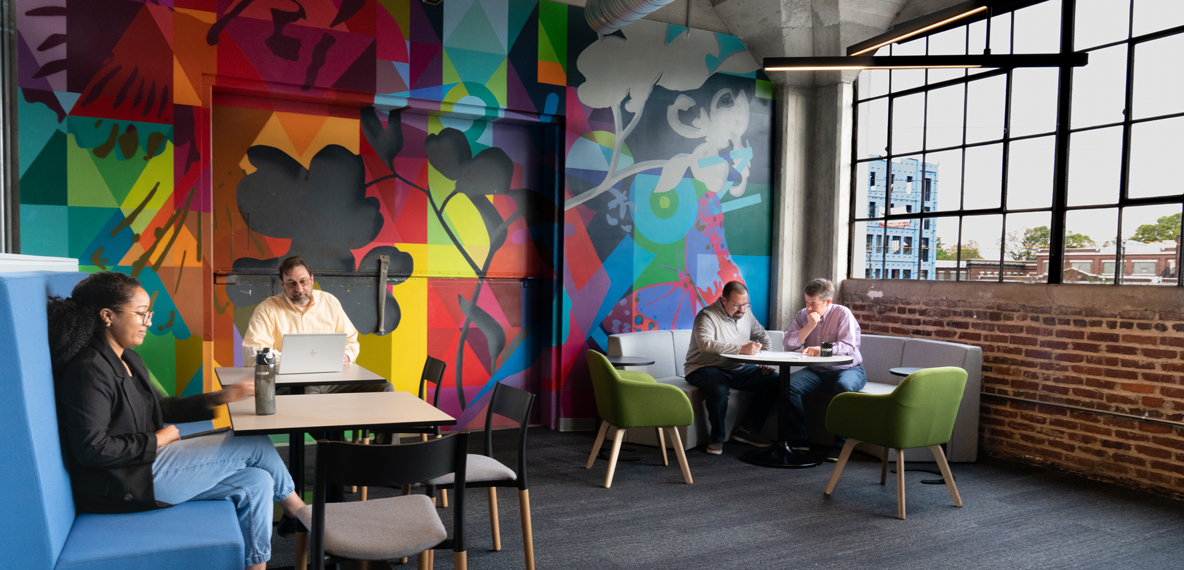 BHDP employees work in the Commons—a collaborative space backed by a colorful mural. 