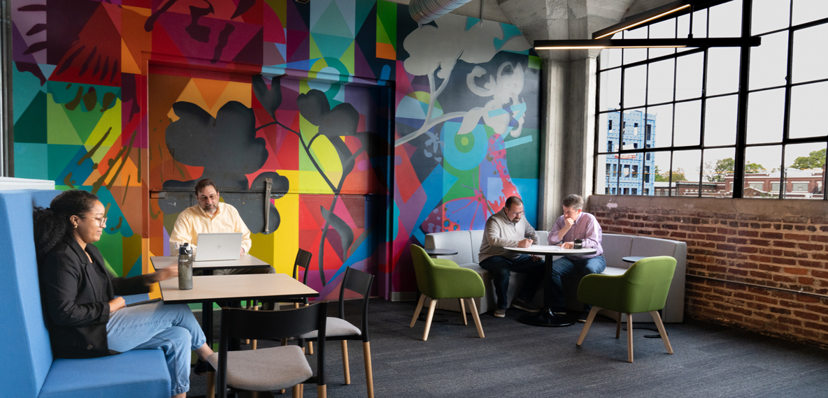BHDP employees work in the Commons—a collaborative space backed by a colorful mural.