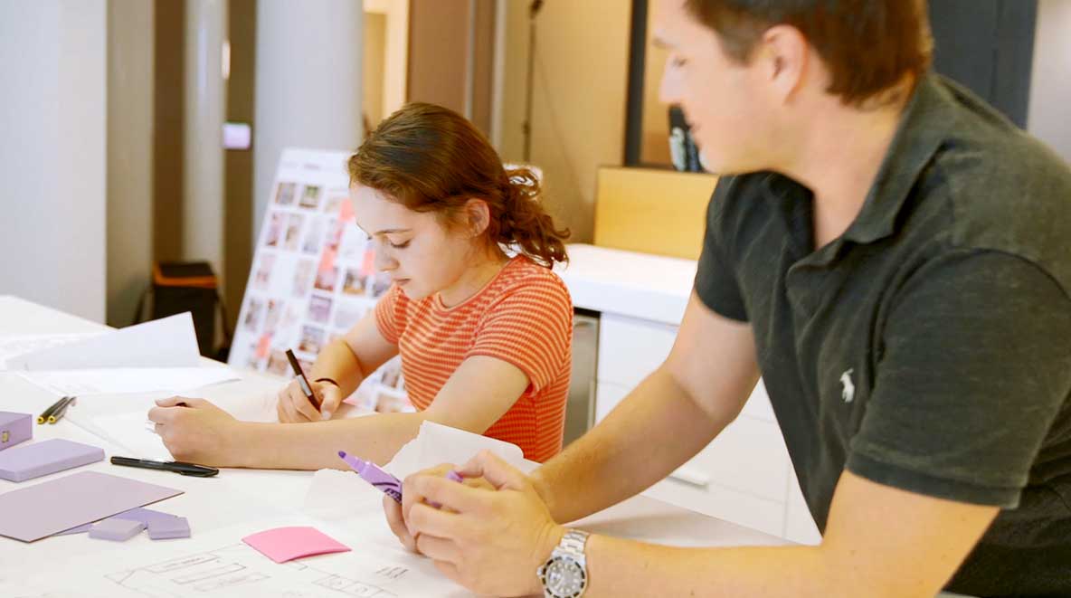 A young girl sits at a table with an architect and sketches ideas