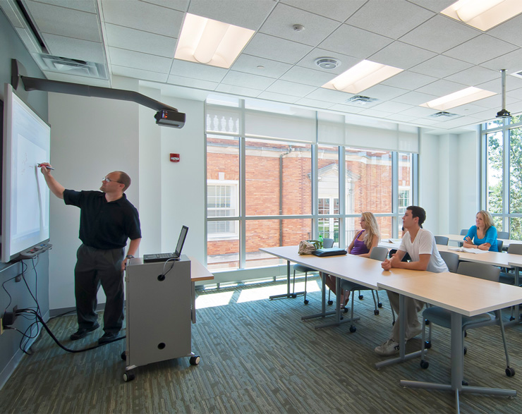 A teacher works on a projector at the front of the class