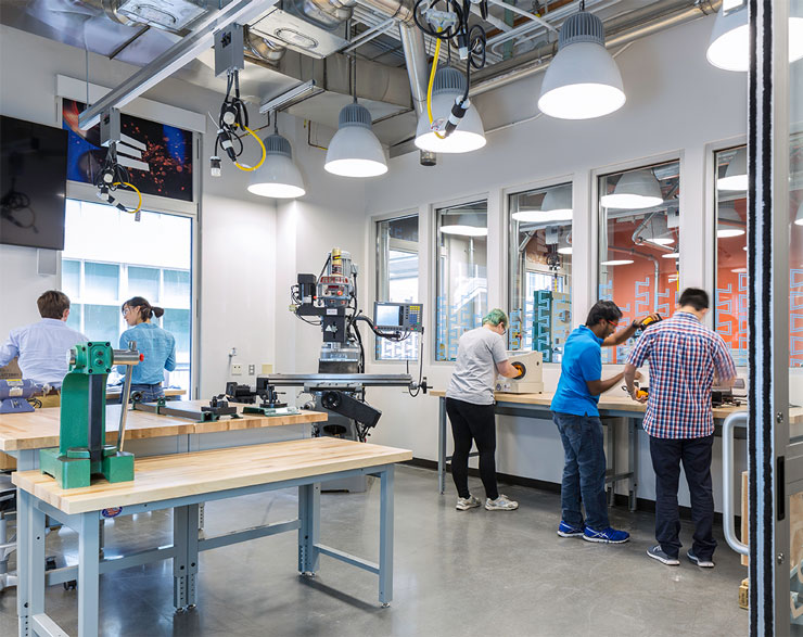 Students collaborate at work benches on the perimeter of the lab