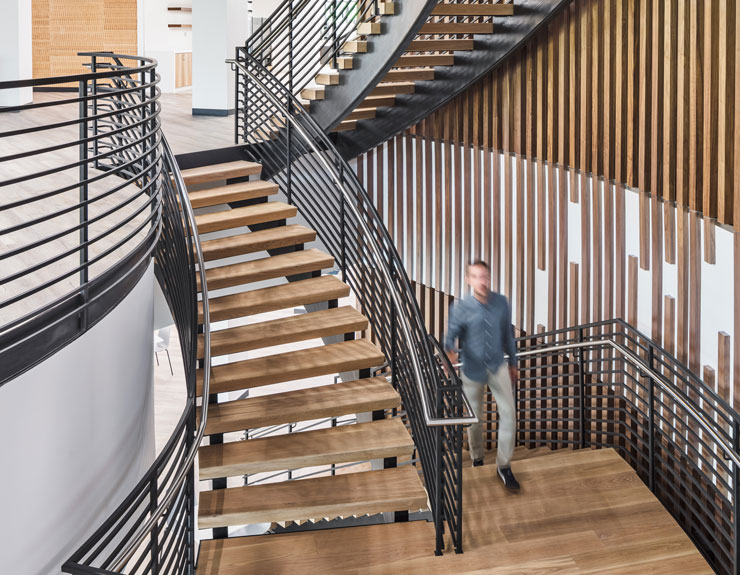 An employee advances from one floor to the next using a staircase with wooden accents