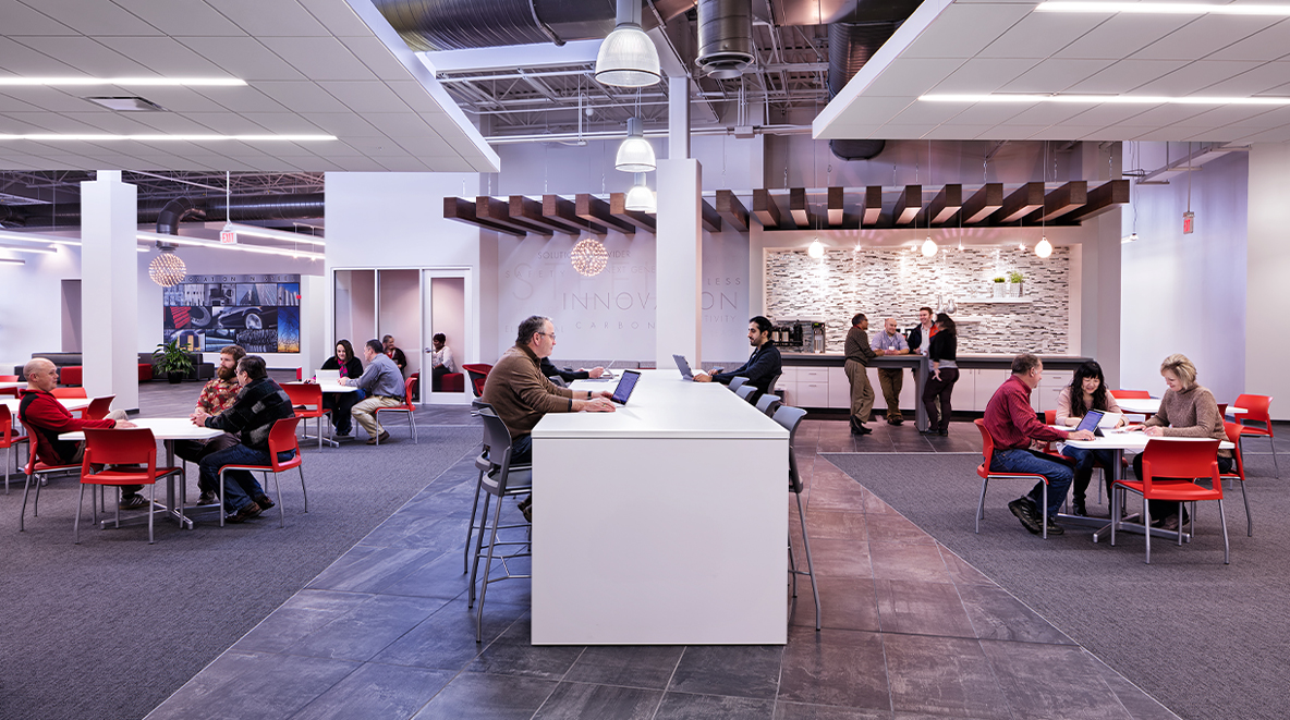 Employees work in an open collaboration space with tables and chairs