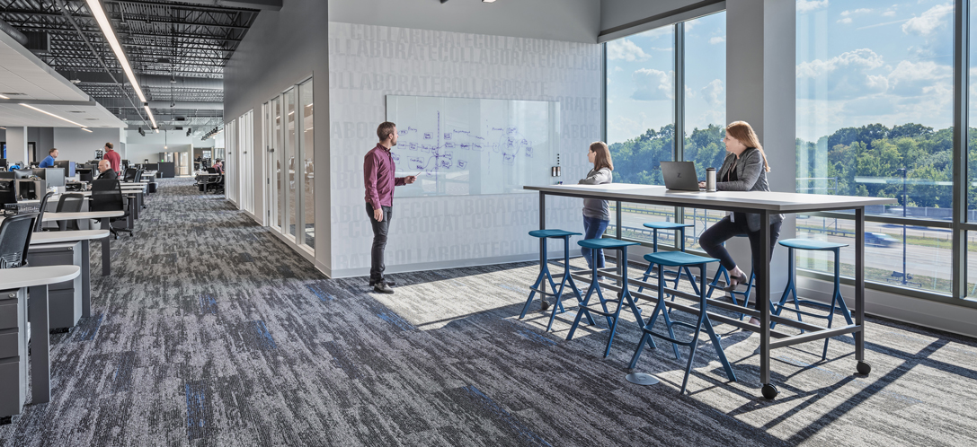 Employees collaborate at a high-top table using a white board on a nearby wall