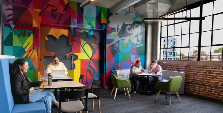 Employees work together in the Commons—a collaborative space backed by a colorful mural. 