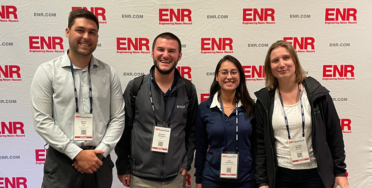 Adam and Michael stand with two other conference attendees in front of a white backdrop with the ENR logo