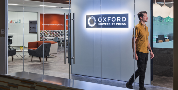 An employee walks by an illuminated sign with the Oxford University Press' logo