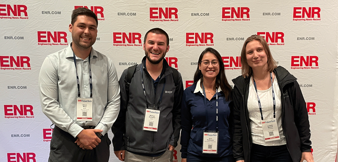 Adam and Michael stand with two other conference attendees in front of a white backdrop with the ENR logo