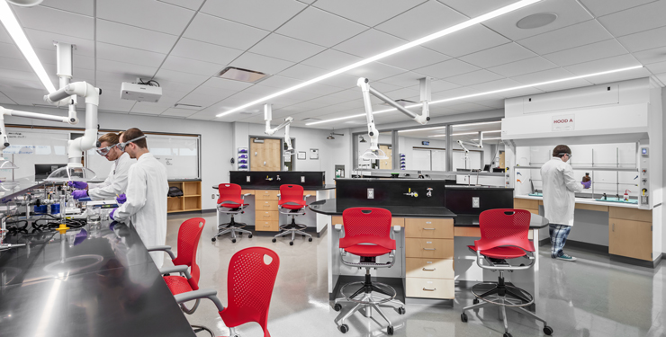 Two students work together in a lab while another student works beside a fume hood