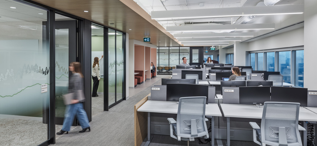 Open desk workstations and glass-walled meeting rooms at P&G Toronto General Office, with employees walking through the space.