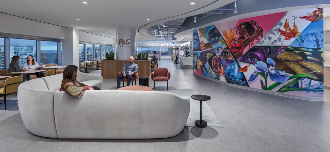 Employees seated in a lounge area at P&G Canada, with a large colorful mural and floor-to-ceiling windows in the background.