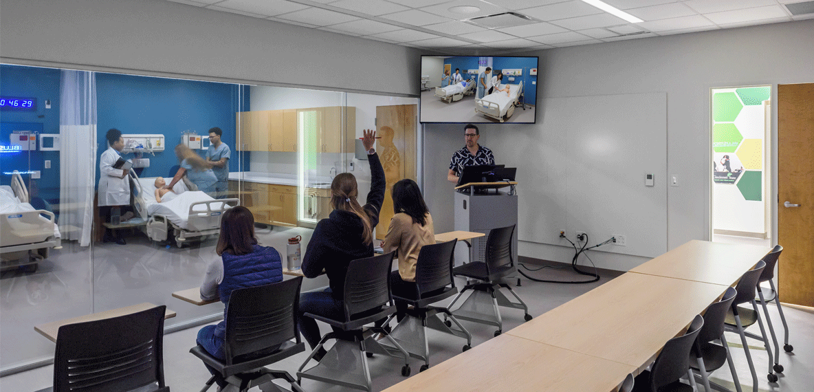 Students immersed in a nursing simulation environment, observing hands-on practice sessions where nurses refine their skills in a controlled setting.