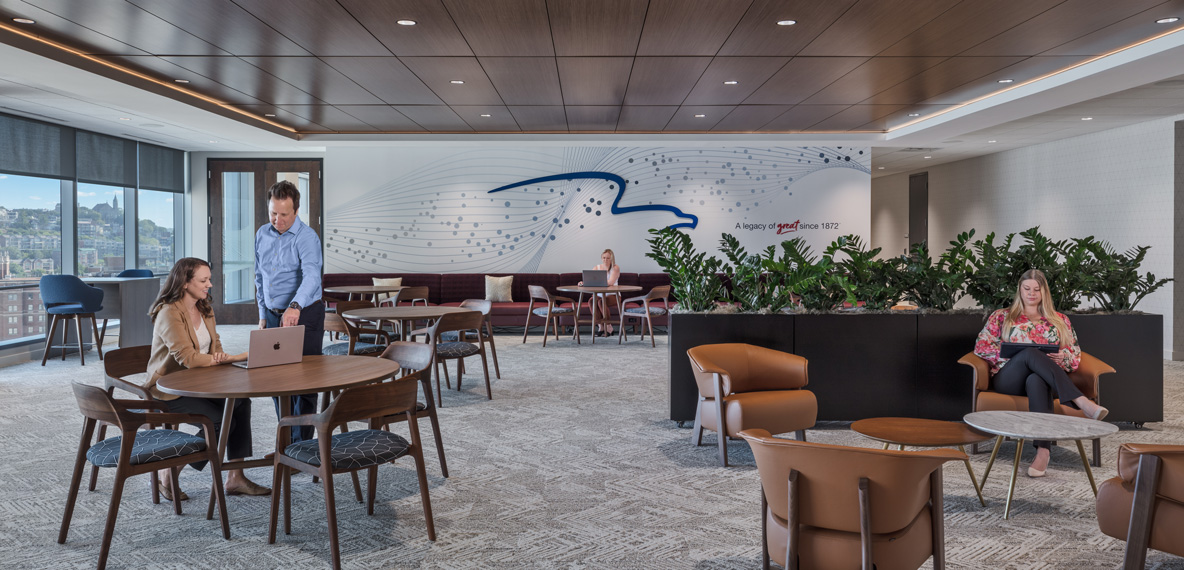 Open workspace at Great American Insurance Group's Cincinnati office with wood-slat ceilings, a wave-patterned feature wall, and employees working at communal tables and lounge seating.