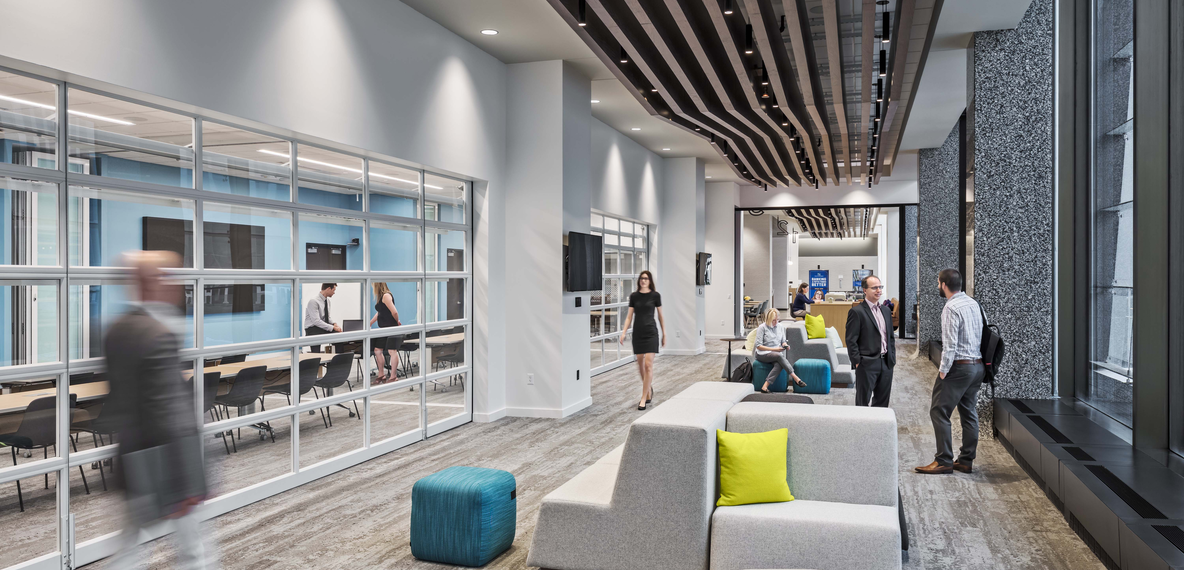 Employees walking and gathering in a modular seating area at Fifth Third's Exchange, with glass-walled meeting rooms and a wood slat ceiling.