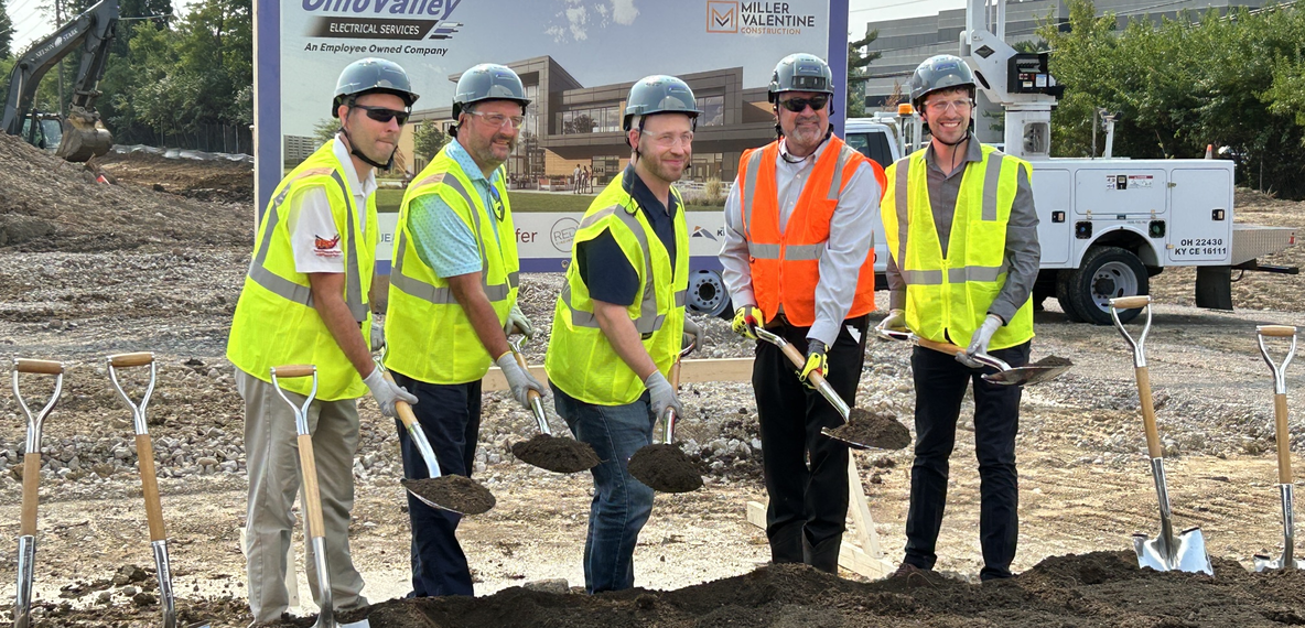 Group of men in hard hats and construction vests posing for image during breaking ground ceremony.