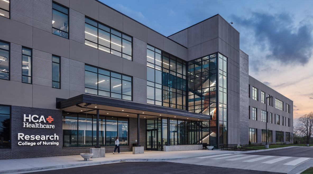 Exterior of the HCA Healthcare Research College of Nursing building at dusk, with a glass-and-brick facade and lit windows.