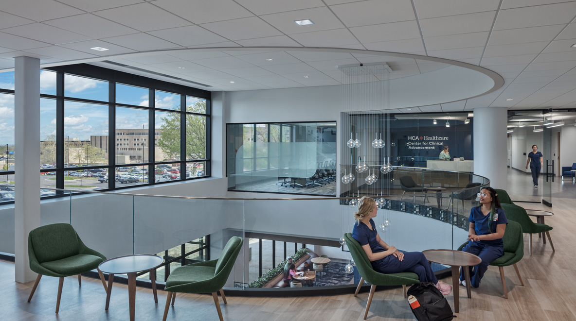 Curved second-floor lounge overlooking the lobby of HCA Healthcare's Center for Clinical Advancement, with staff seated near tall windows.