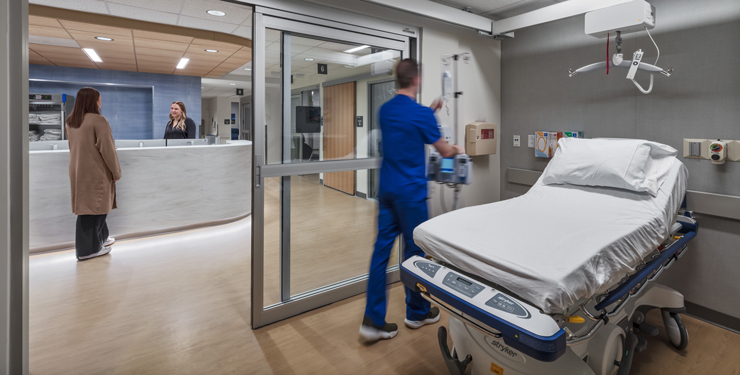 Nurse in room and people talking at desk