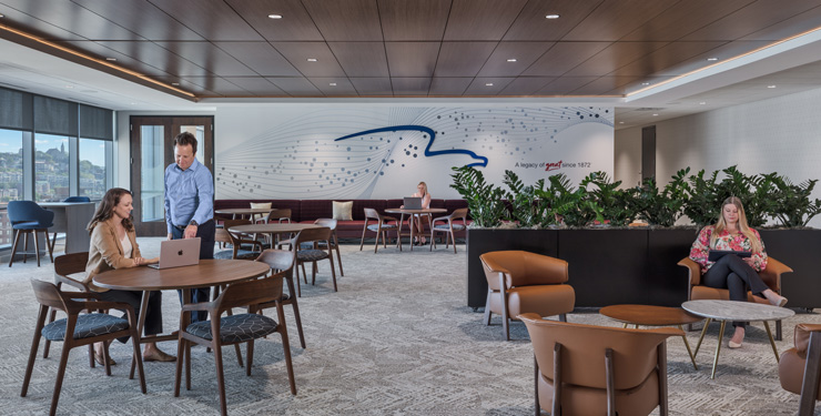 Open workspace at Great American Insurance Group's Cincinnati office with wood-slat ceilings, a wave-patterned feature wall, and employees working at communal tables and lounge seating.