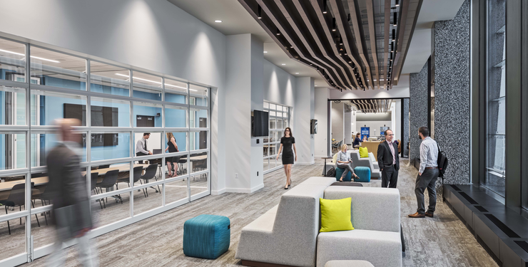 Employees walking and gathering in a modular seating area at Fifth Third's Exchange, with glass-walled meeting rooms and a wood slat ceiling.