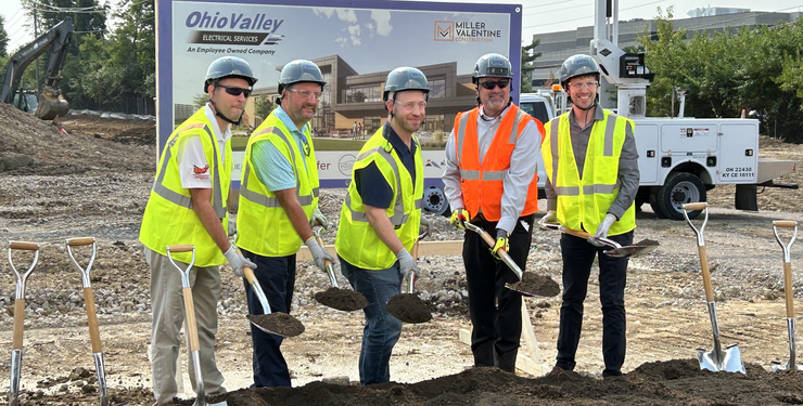 Group of men in hard hats and construction vest posing for image at a breaking ground ceremony.