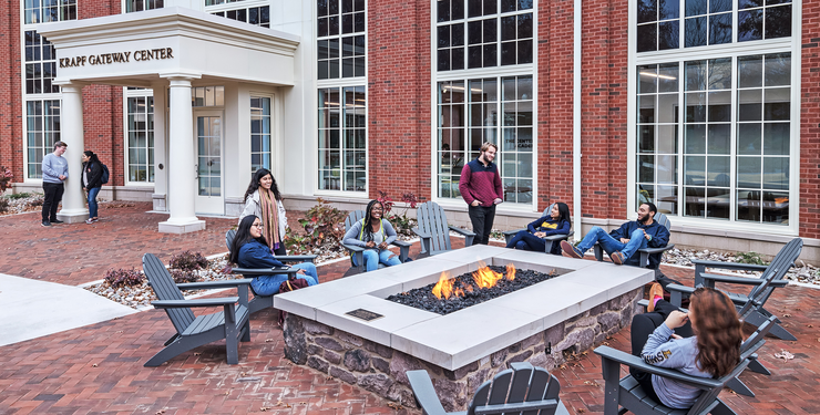 Group of students sitting around a firepit in front of a college building