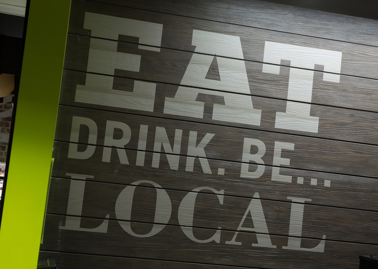 "Eat Drink. Be... Local" experiential graphics on a wood panel wall in Brothers Marketplace Medfield, MA