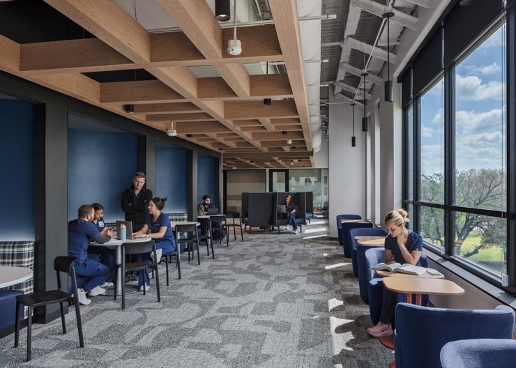 Student lounge with exposed wood beams, group seating for study sessions, and window nooks for individual studying.
