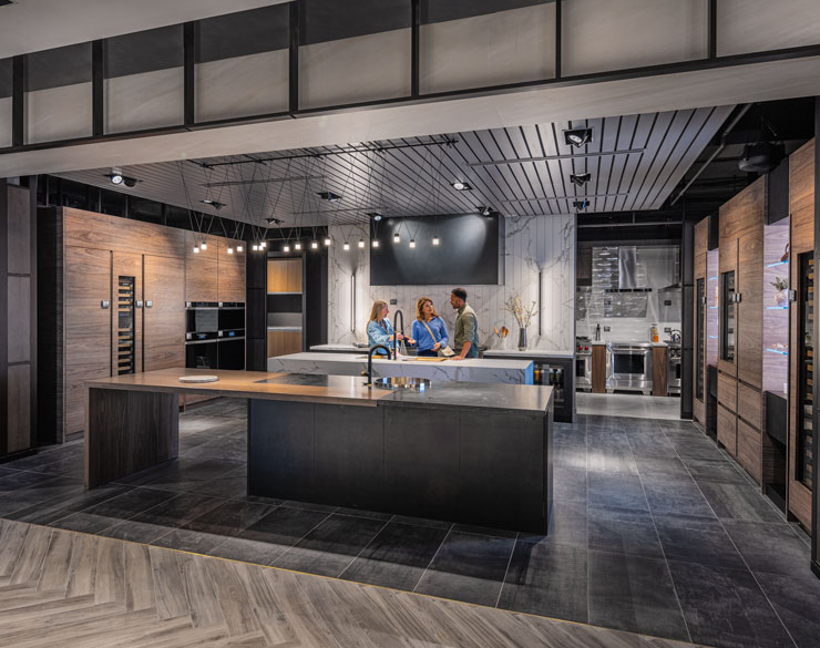 Customer, architect, and employee discussing products in a dark-themed kitchen display at Ferguson Studio Showroom