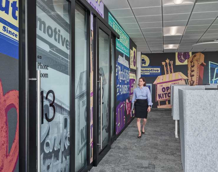 Employee walking past EGD-covered huddle rooms at WTW's Charlotte office