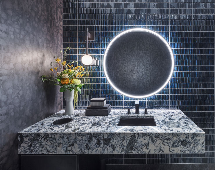 Mirror with a bight light around it. Marble sink underneath with bright yellow flowers on it.
