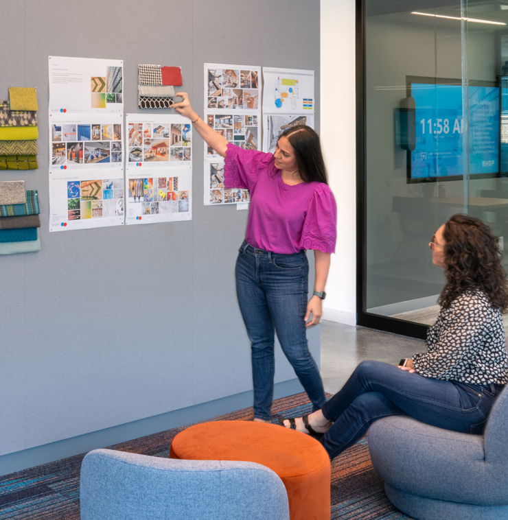 Two employees look at colorful images pinned up on a grey wall