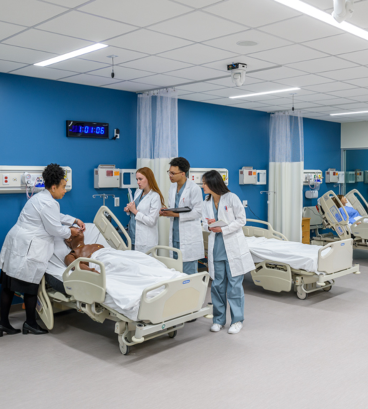Three students watch their instructor as she demonstrates patient care.